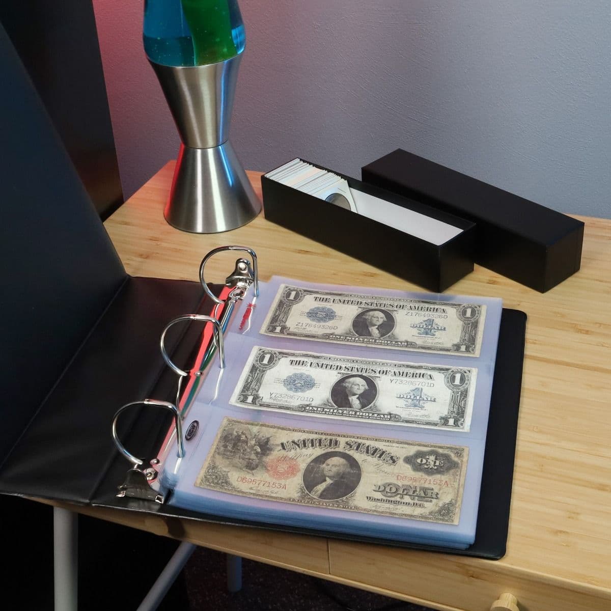 : BCW LaserWeld 3-pocket currency pages displayed in a 3-ring binder on a desk, showcasing organized and protected banknotes alongside collector storage accessories.