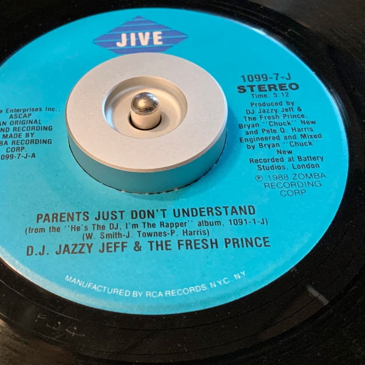 BCW 7 Inch Record Player Adapter - Classic in use with a 7-inch vinyl record of 'Parents Just Don’t Understand' by DJ Jazzy Jeff & The Fresh Prince. The silver aluminum adapter is fitted securely in the center hole of the record, providing stability on th