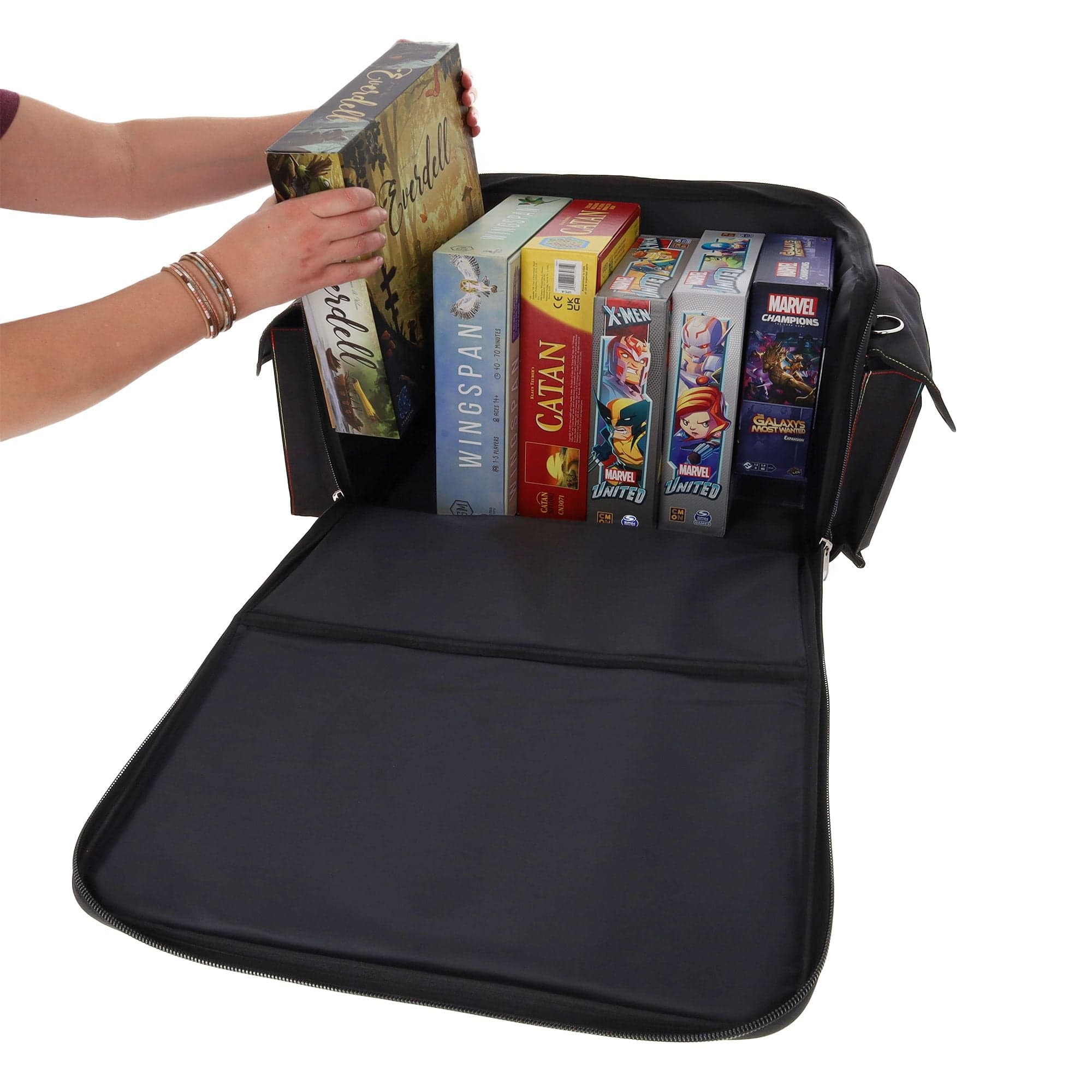 black BCW Board Game Bag being used to store several board games. The bag's top is unzipped and laid open, revealing the interior space, which can accommodate approximately six to eight standard-sized board games. A person is pulling a board game out of i