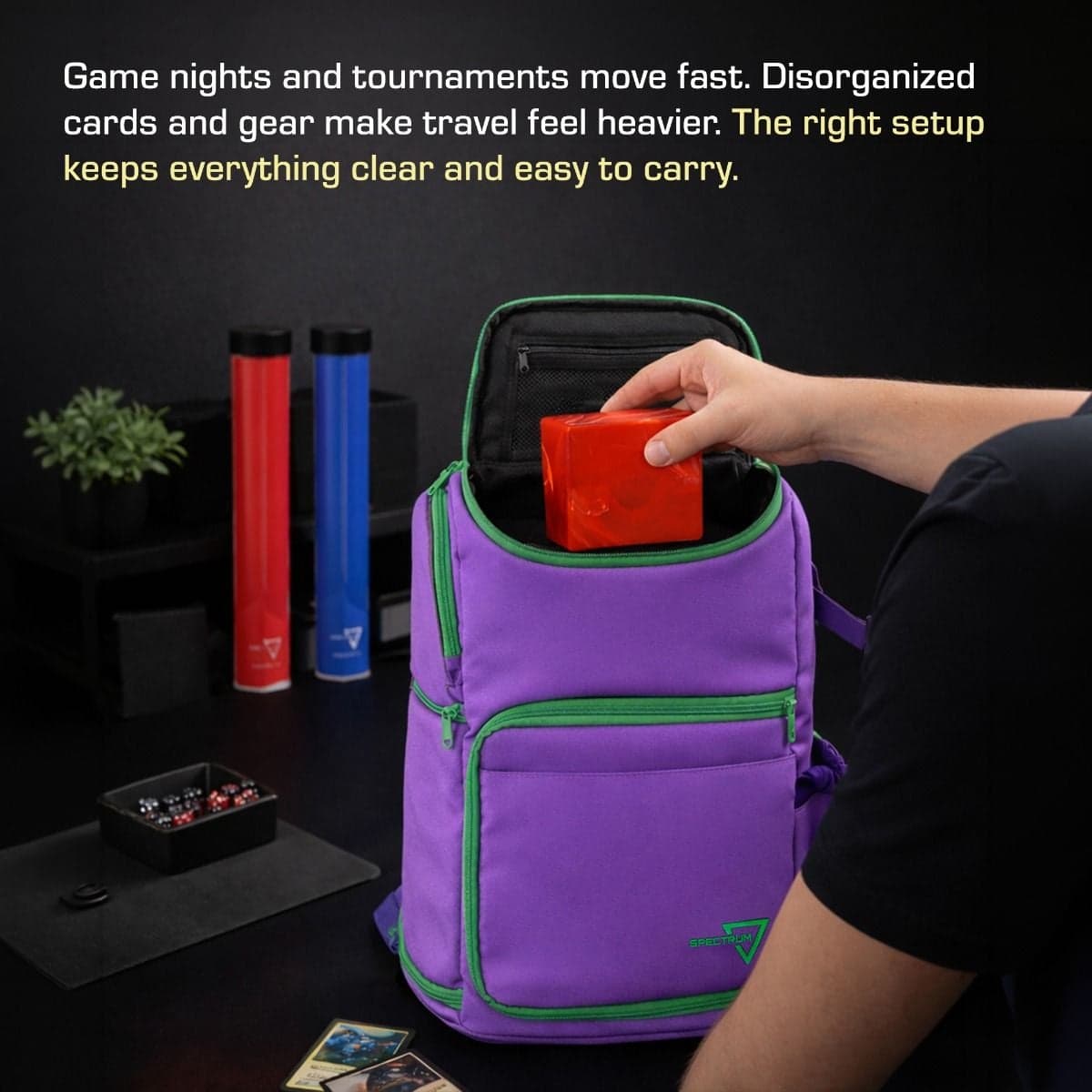 Spectrum Backpack Infographic showing hand inserting red box into gamma purple backpack, bag sitting on table, gaming equipment sitting in the background. The top of the image contains the text "Game nights and tournaments move fast. Disorganized cards an