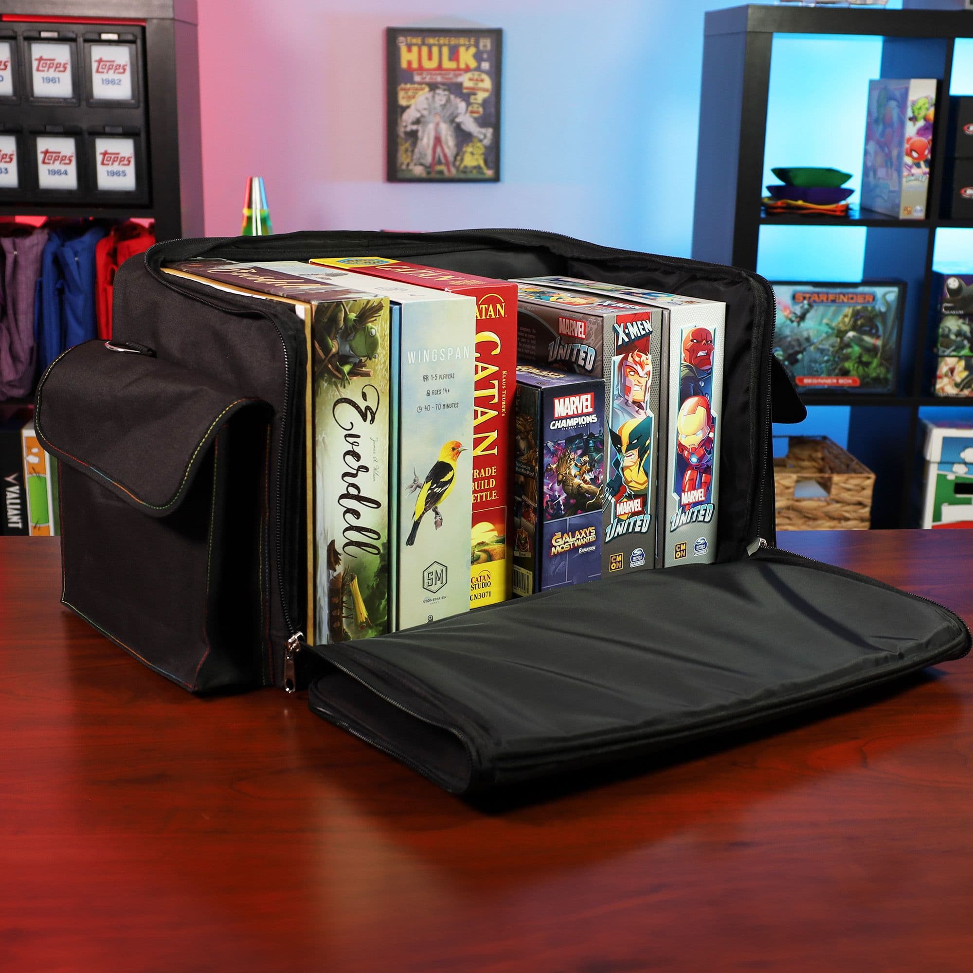 the BCW Board Game Bag in black, placed on a wooden tabletop with the top unzipped and laid open to reveal its contents. Several board games are neatly organized inside the bag.