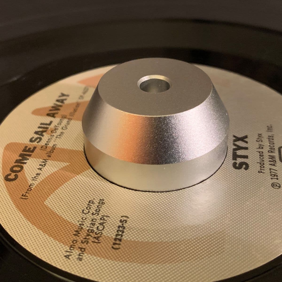 BCW 7 Inch Record Player Adapter - Dome in use with a 7-inch vinyl record of 'Come Sail Away' by Styx. The silver, dome-shaped aluminum adapter fits snugly in the center hole, ensuring stability on the turntable. The A&M Records label with its classic des