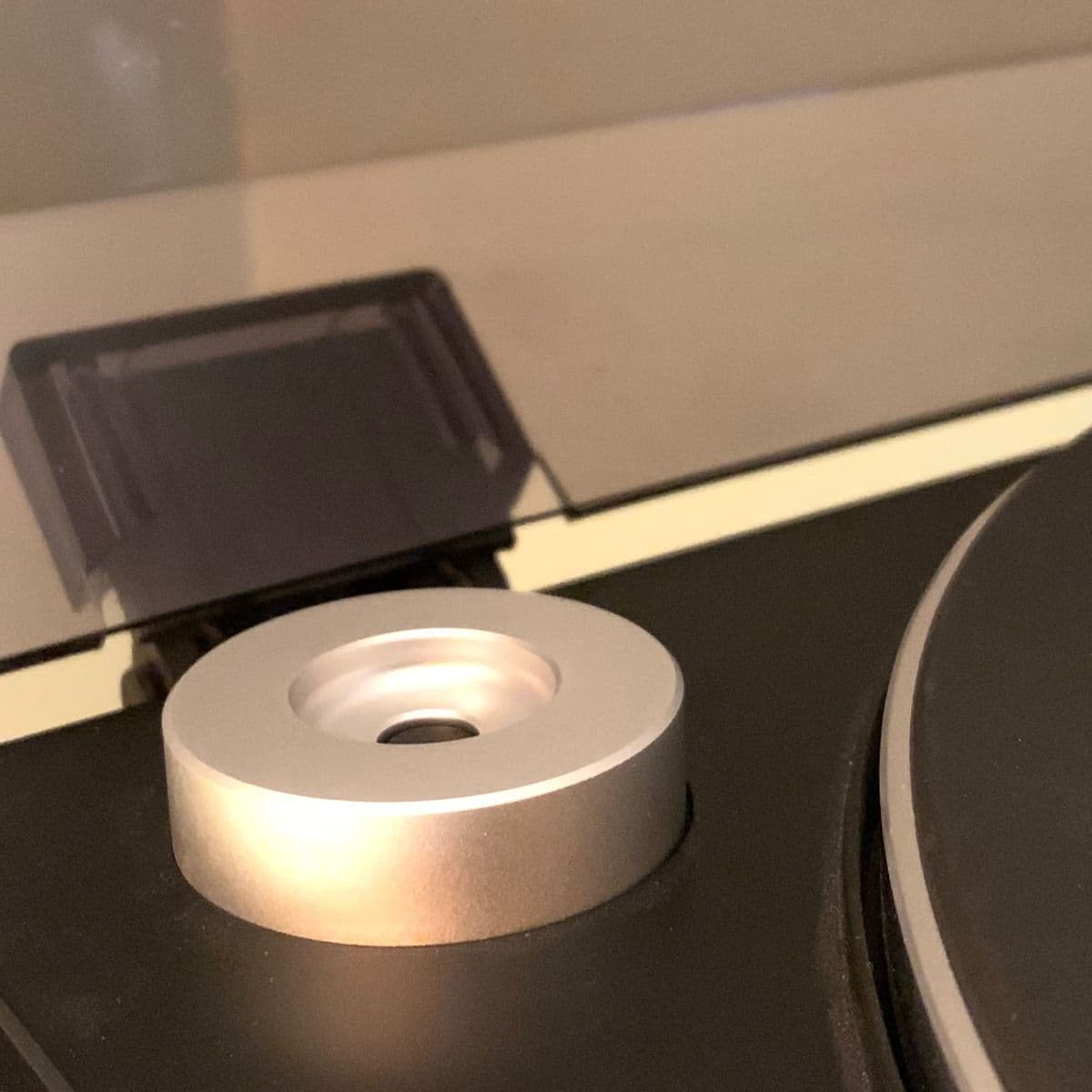BCW 7 Inch Record Player Adapter - Classic, resting on a turntable platform. The silver aluminum adapter is designed to fit the center hole of 7-inch records, ensuring stable playback. Its sleek and compact design complements the turntable setup.