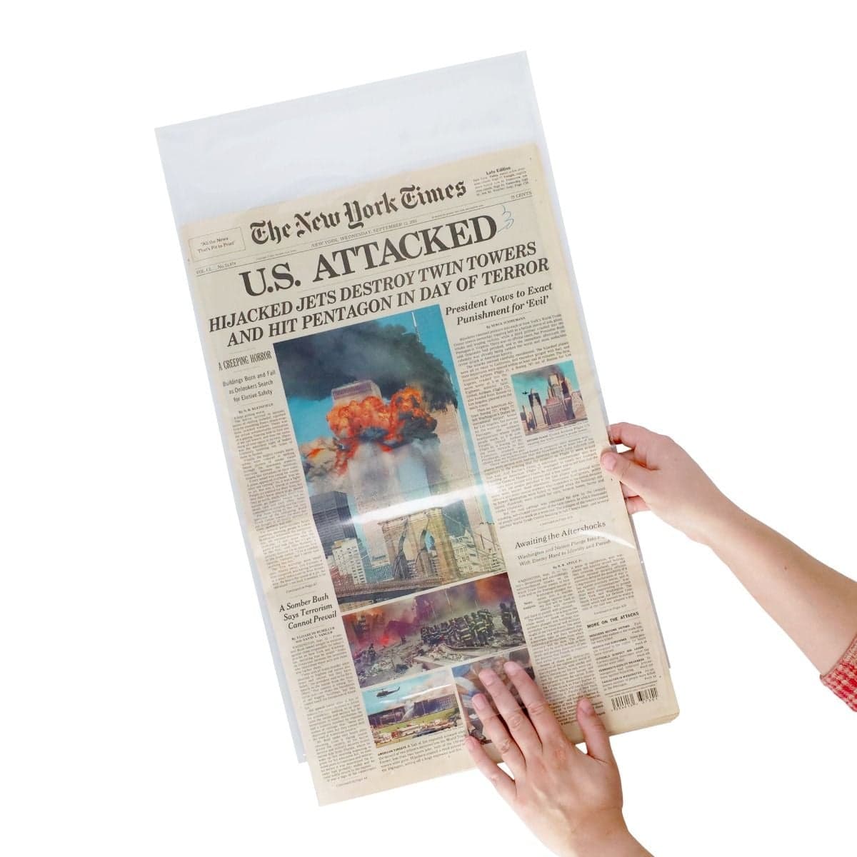Hands inserting and positioning a historic newspaper inside a clear BCW polypropylene sleeve for protective storage and preservation.