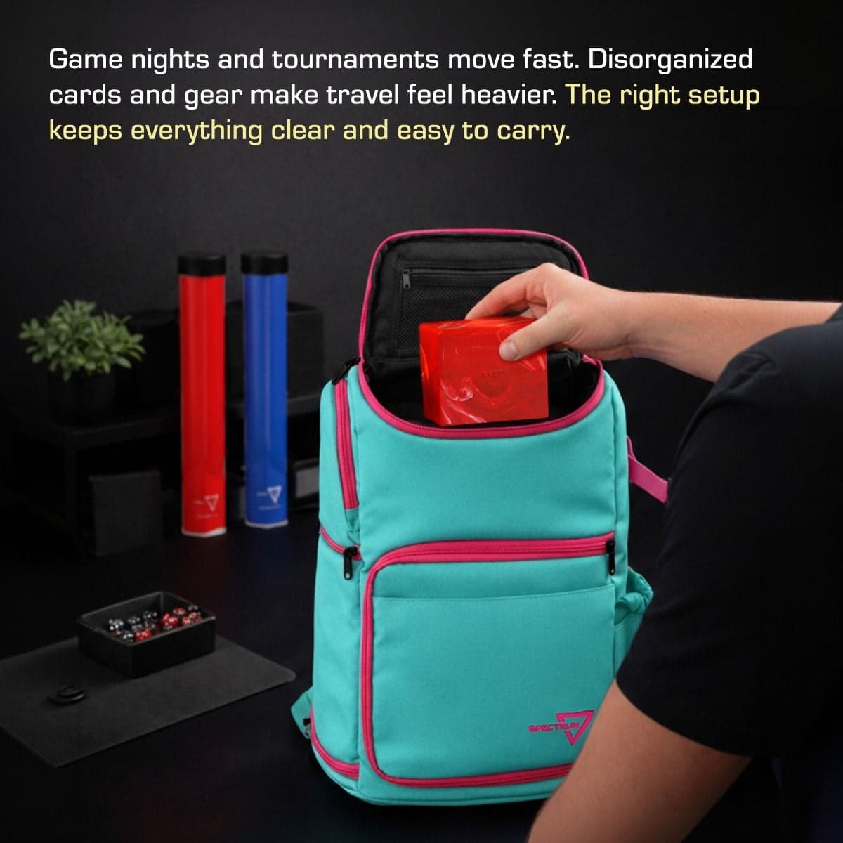 Spectrum Backpack Infographic showing hand inserting red box into gamma purple backpack, bag sitting on table, gaming equipment sitting in the background. The top of the image contains the text "Game nights and tournaments move fast. Disorganized cards an