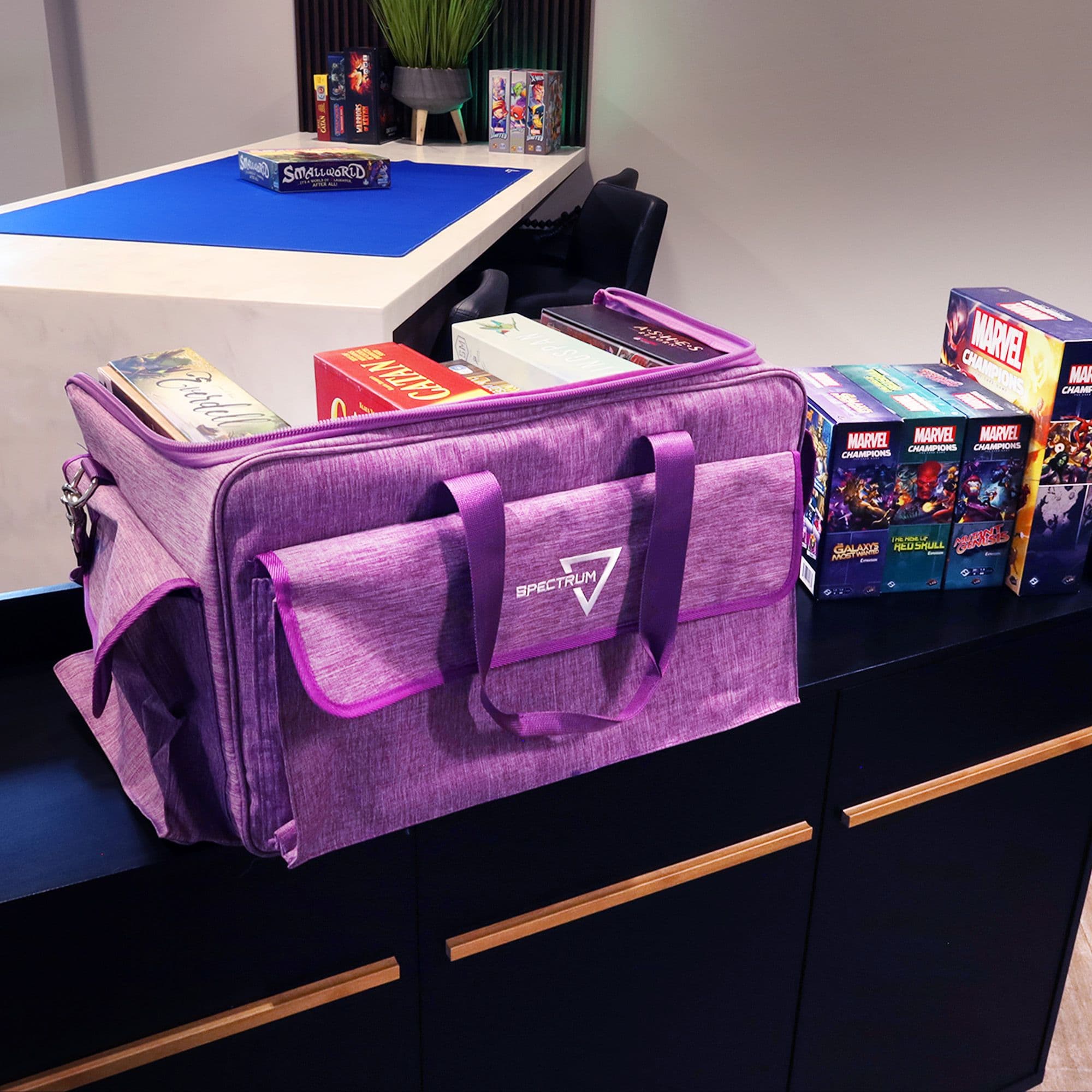 the BCW Board Game Bag in purple, placed on a wooden tabletop with the top unzipped and laid open to reveal its contents. Several board games are neatly organized inside the bag.