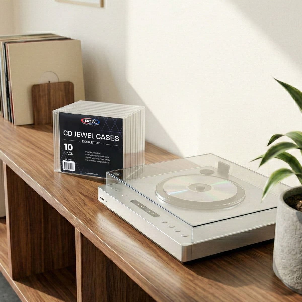 BCW CD Jewel Cases Double Tray 10 pack stacked front to back on a wooden shelf, next to a professional CD player