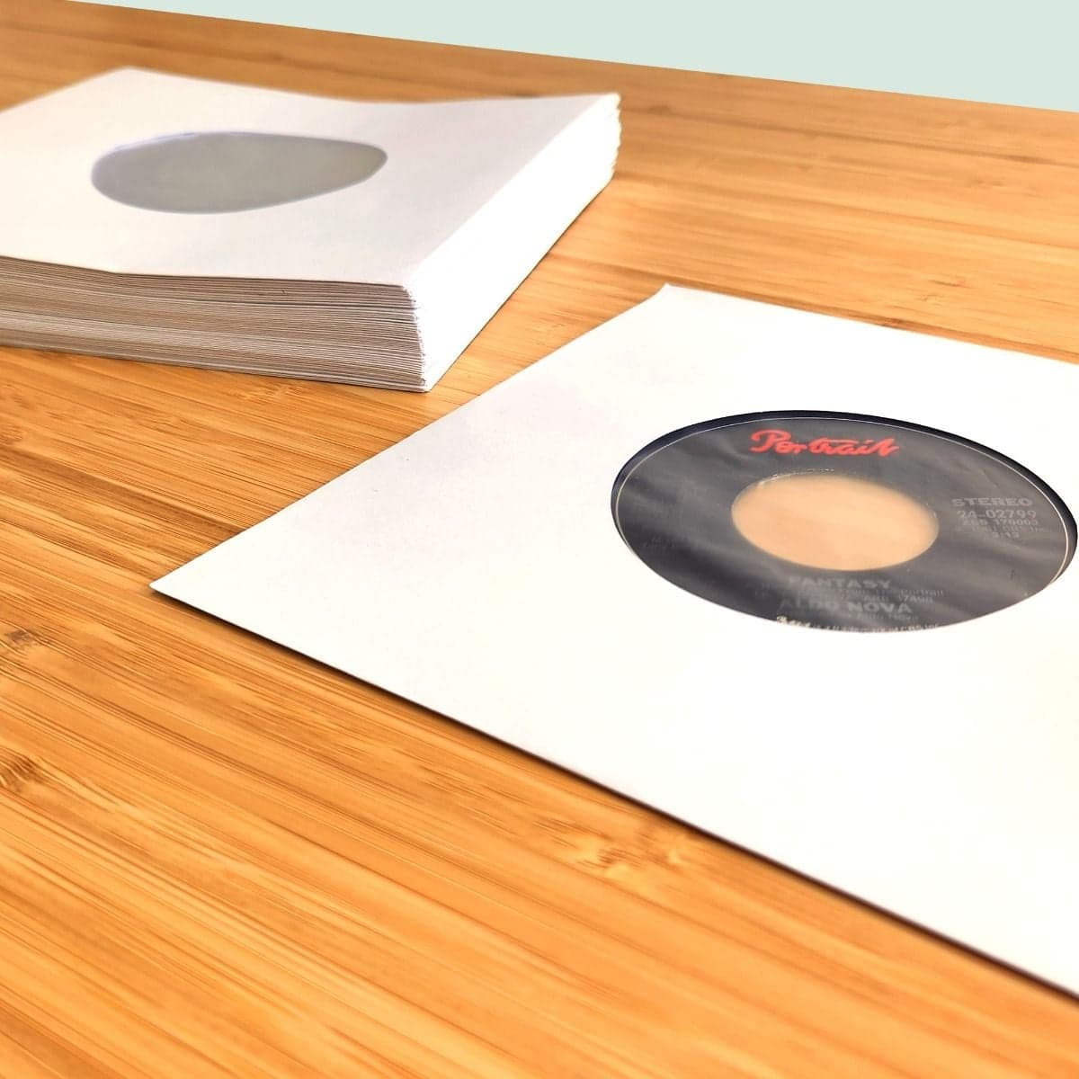 Stack of BCW 7 Inch Record Paper Inner Sleeves - Polylined - With Hole - White next to record in sleeve