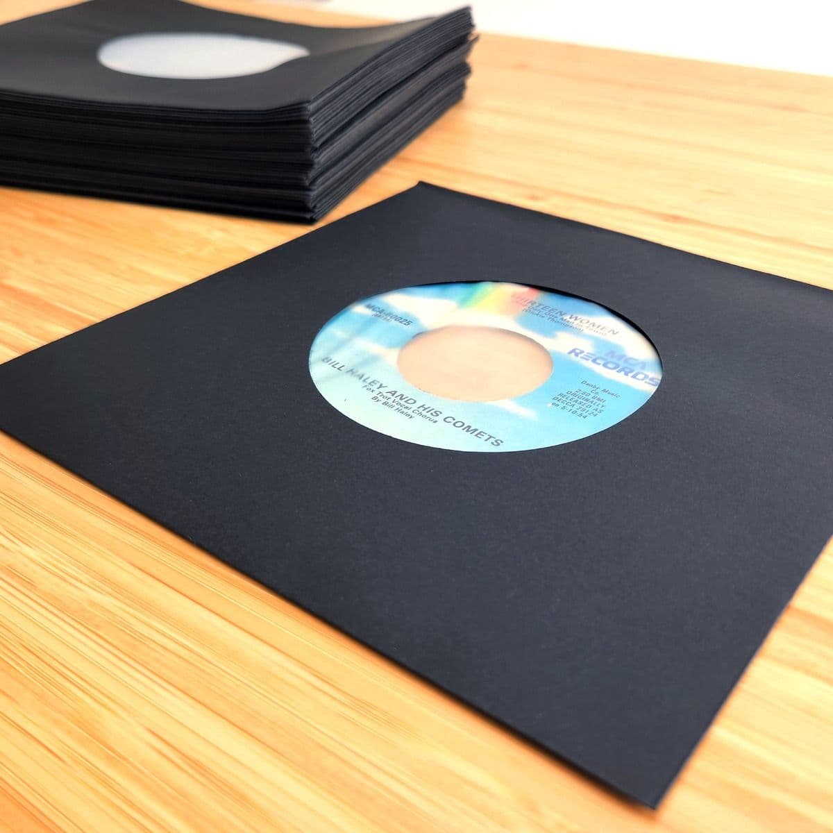 Stack of BCW 7 Inch Record Paper Inner Sleeves - Polylined - With Hole - Black next to record in sleeve