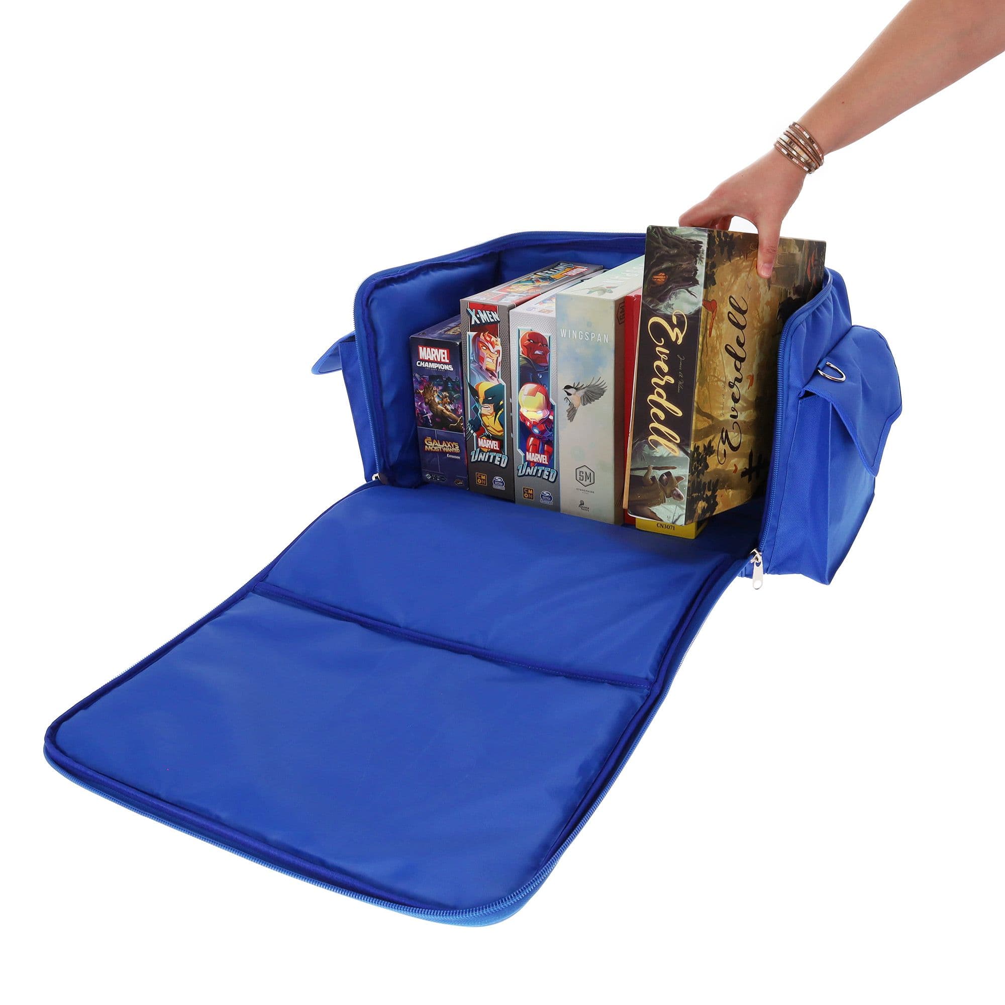 blue BCW Board Game Bag being used to store several board games. The bag's top is unzipped and laid open, revealing the interior space, which can accommodate approximately six to eight standard-sized board games. A person is pulling a board game out of it