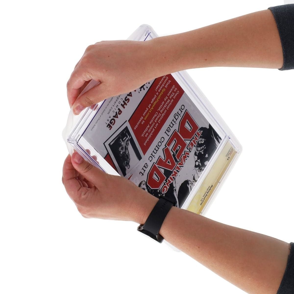 a person applying a BCW Graded Comic Slab Bumper onto a graded comic book slab. The hands are positioning the translucent rubber bumper around the edges of the slab, providing a snug fit for added protection.