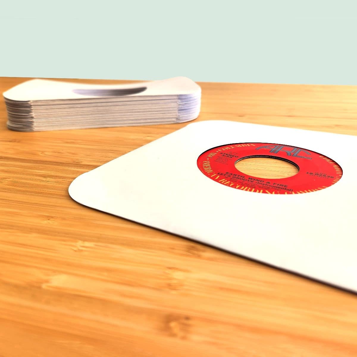 Stack of BCW 7 Inch Record Paper Inner Sleeves - Round Corners - With Hole - White next to record in sleeve