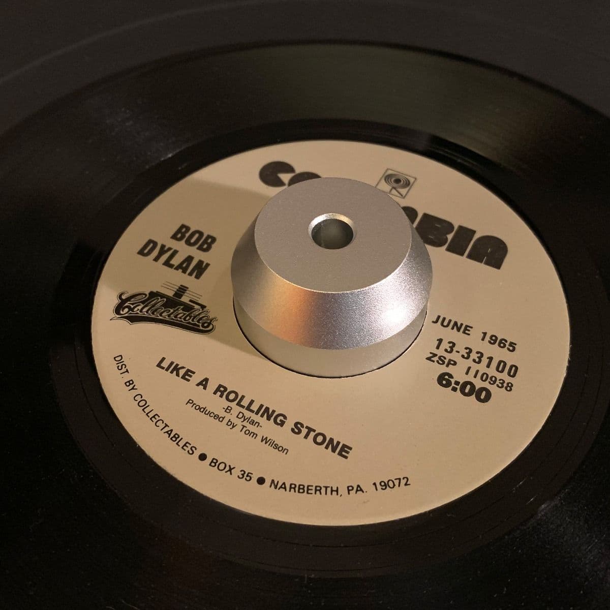 BCW 7 Inch Record Player Adapter - Dome in use with a 7-inch vinyl record of 'Like a Rolling Stone' by Bob Dylan. The silver, dome-shaped aluminum adapter fits securely in the center hole of the record, ensuring stability on the turntable. The classic Col