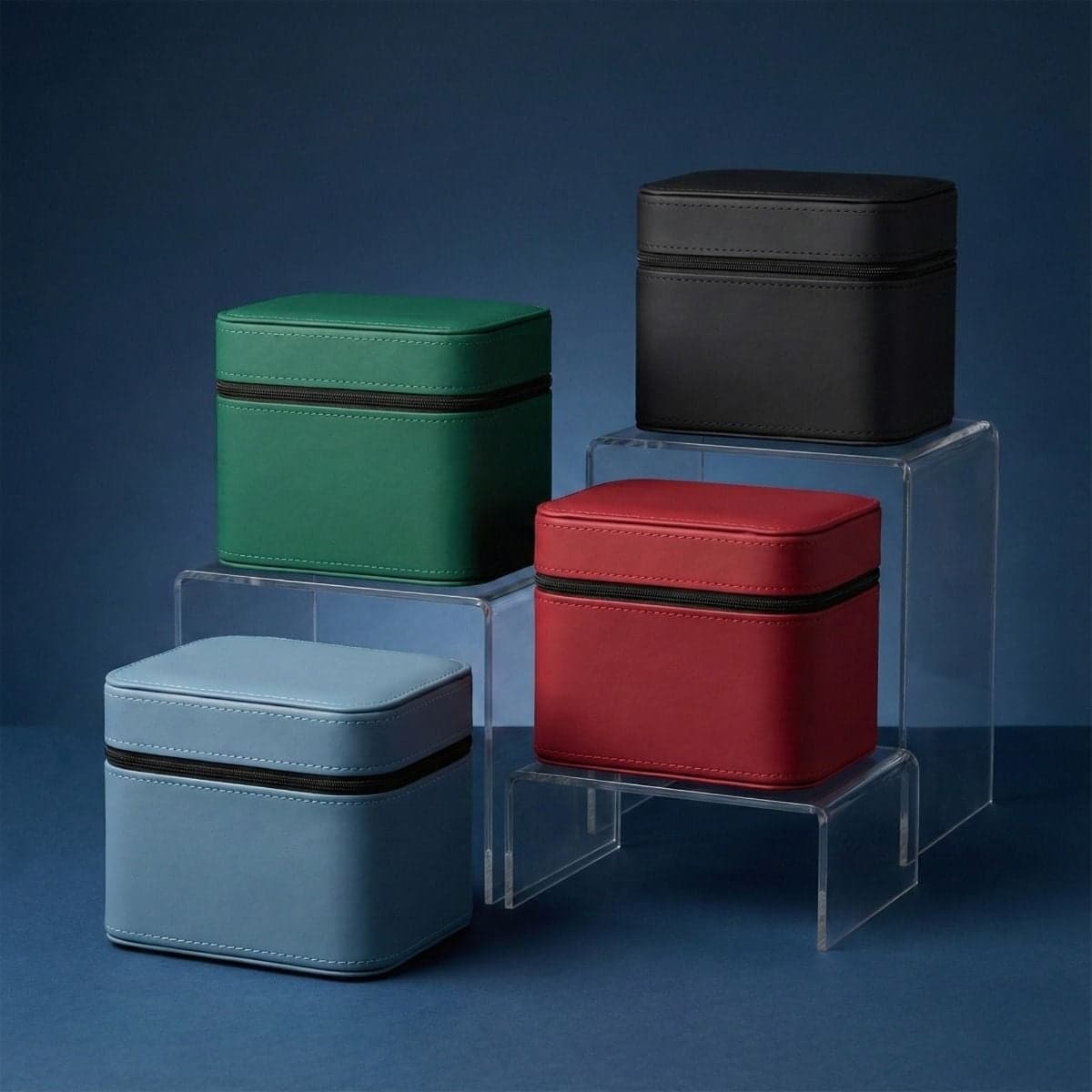 Four compact zippered trading card storage cases displayed on clear risers, shown in black, red, green, and light blue against a dark blue background.